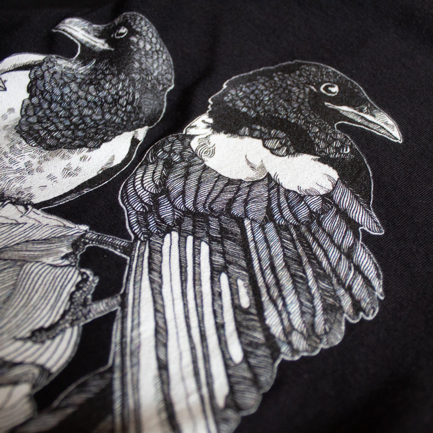 Close-up on black and white, tattoo inspired, gothic, witchy, pagan art on clothing piece. Birds & Bones collection features nature and death inspired artwork on t-shirts and sweathirts.